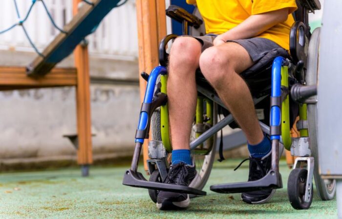 صبي مصاب بالشلل يجلس على كرسي متحركة لها دواليب وهو موجود في ساحة للعب الأطفال