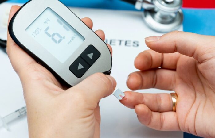 شخص بالغ يرتدي خاتما يقوم بفحص مستوى السكر في الدم لديه عن طرق جهاز كشف عن مستوى السكر لونه أبيض وذلك من خلال وضع قطرة من الدم الحمراء فيه