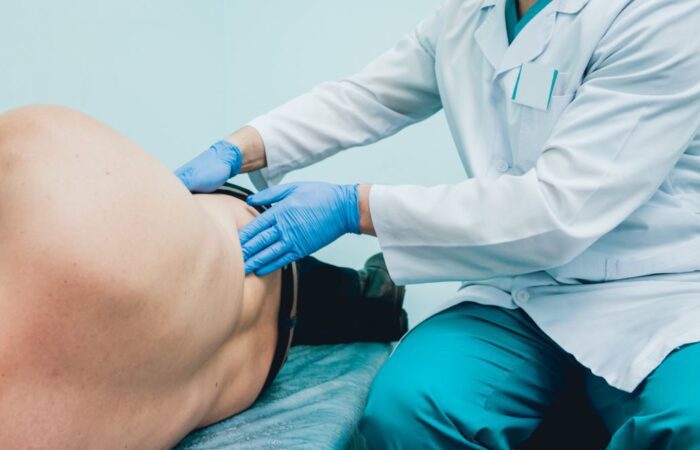 طبيب يقوم بفحص خاصرة مريض مستلقي على السرير في العيادة الطبيبة