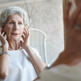 امرأة مسنة لون شعرها أبيض تنظر لنفسها في المرآة