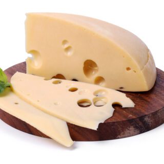 قرص جبنة أصفر اللون على لوح خشبي بني وبجانب القرص ورقة نباتية خضراء