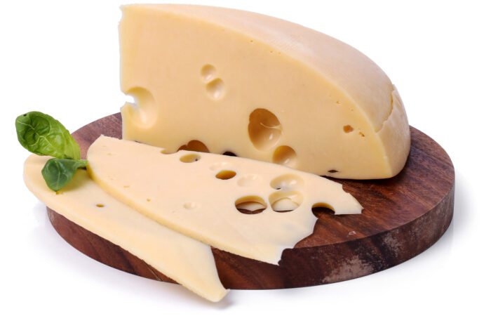 قرص جبنة أصفر اللون على لوح خشبي بني وبجانب القرص ورقة نباتية خضراء