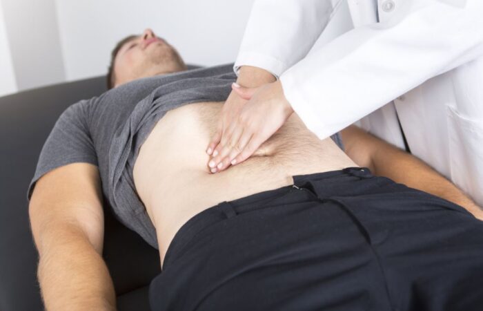 طبيب يقوم بالضغط على بطن مريض مستلقي على السرير