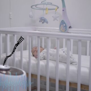 طفل رضيع ينام في سريره الأبيض وبجانبه آلة تصدر أصوات خفيفة مختلفة