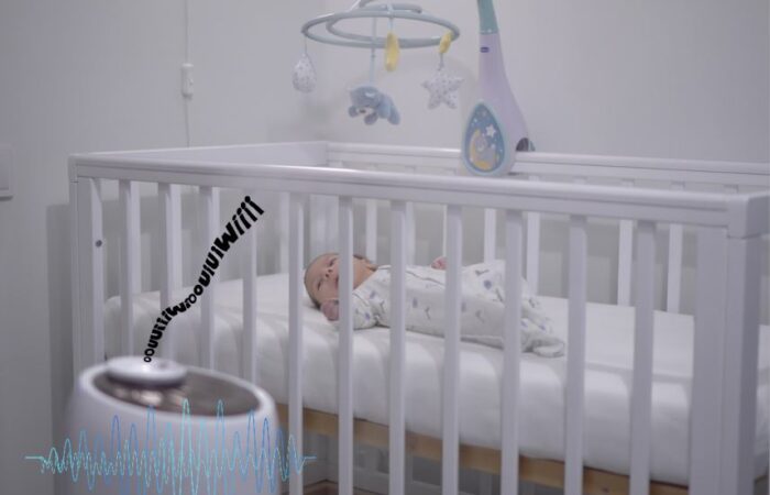 طفل رضيع ينام في سريره الأبيض وبجانبه آلة تصدر أصوات خفيفة مختلفة