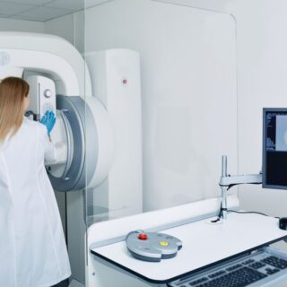 طبيبة نسائية تستخدم جهاز طبي كبير ومن خلفها تقف مريضة مسنّة تلبس ثوب مخطط بالأبيض والأزرق