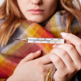 امرأة بالغة تحمل ميزان قياس حرارة الجسم وهي تلبس غطاء شتوي