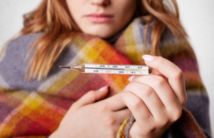 امرأة بالغة تحمل ميزان قياس حرارة الجسم وهي تلبس غطاء شتوي