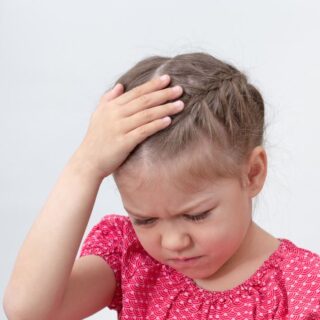 فتاة صغيرة ترتدي كنزة زهرية تظهر متعبة وتضع يدها اليمين على رأسها وهي تنظر للأسفل