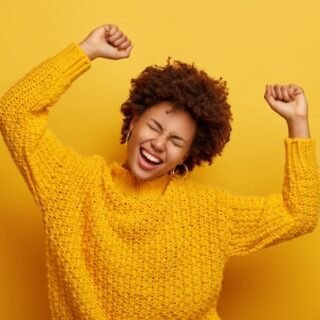 امرأة تلبس كنزة صفراء تصرخ بسعادة وترفع يديها للأعلى