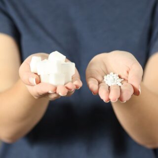 فتاة تمسك بمكعبات من السكر في يدها اليمين وفي يدها اليسار يوجد حبات السكرين