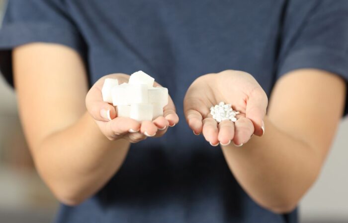 فتاة تمسك بمكعبات من السكر في يدها اليمين وفي يدها اليسار يوجد حبات السكرين