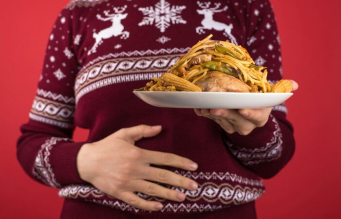 امرأة تلبس كنزة خمرية اللون وتحمل صحن طعام يوجد فيه وجبة كبيرة وتضع يدها الأخرى على بطنها