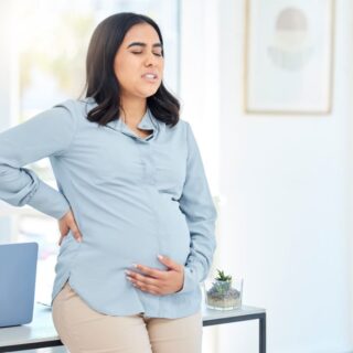 امرأة حامل مغمضة العينين تلبس قميص أزرق وتضع يد خلف ظهرها واليد الآخرى أسفل بطنها