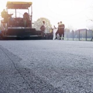 عمال البناء يقومون بمد طبقة سوداء على الطريق باستخدام آلة عريضة صفراء اللون