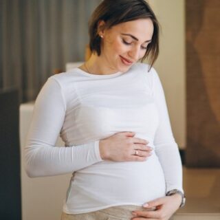 امرأة حامل ترتدي كنزة بيضاء وتضع يديها على بطنها