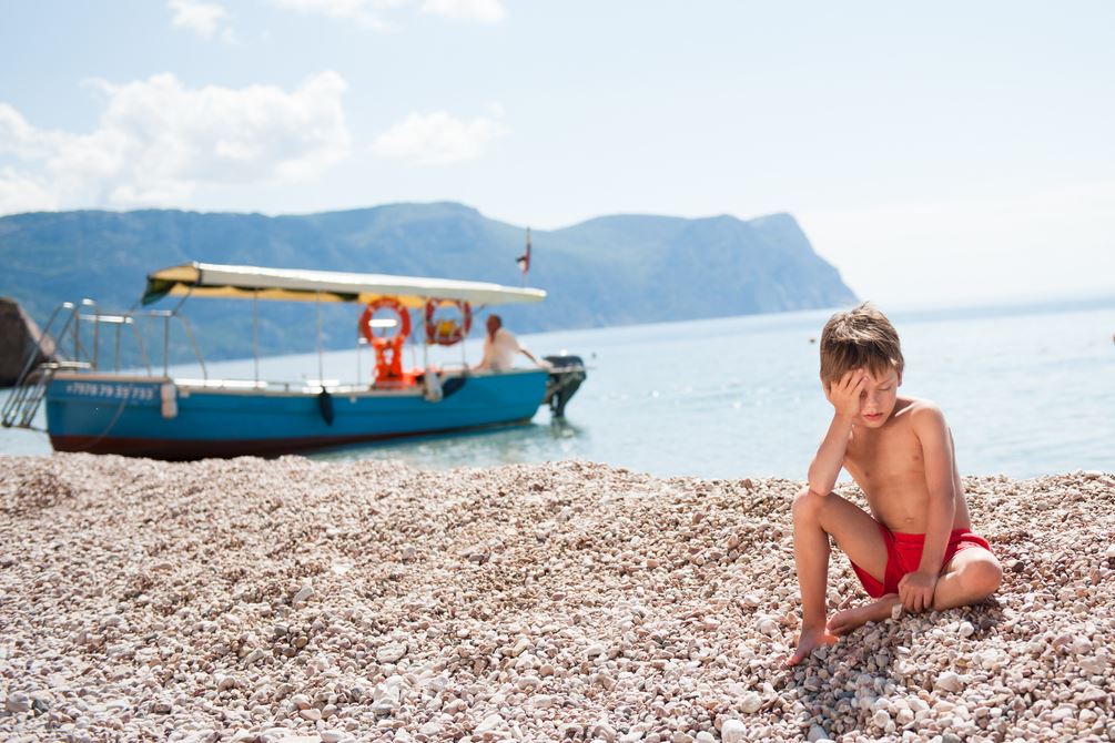 صبي يجلس على الشاطئ وقد أصيب بضربة شمس