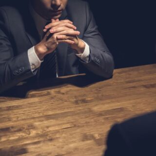 محقق يلبس بدلة رسمية يجلس أمام مجرم في غرفة مظلمة لاستجوابه