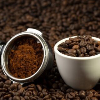 فنجان أبيض بداخله حبيبات بنية داكنة وبجانبه قطعة معدنية دائرية بها طحين بنيّ اللون