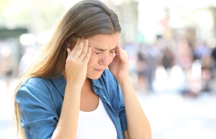 امرأة بالغة تلبس قميص أزرق تضغط بأصابع يديها على رأسها وهي مغمضة العينين