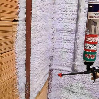 شخص يقوم برش مادة البولي يوريثان الرغوية البيضاء على حائط قرميد بنيّ