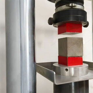 قطعة ميكانيكية ضاغطة تحتوي بين طرفيها على قطعة اسمنتية مكعبة رمادية اللون