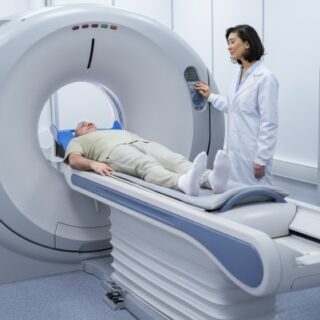 مريض يستلقي على سرير طويل يمرّ بفتحة جهاز طبي اسطواني الشكل وتقف جانبه ممرضة تلبس رداء أبيض