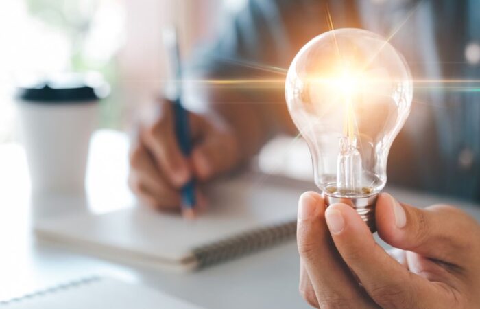 شخص يحمل مصباح مضيئ بيده وباليد الأخرى يقوم بالكتابة على دفتر