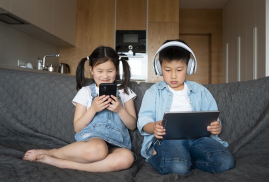 صبي وفتاة يجلسون على الأريكة ويستخدمون أجهزتهم الالكترونية للتسلية