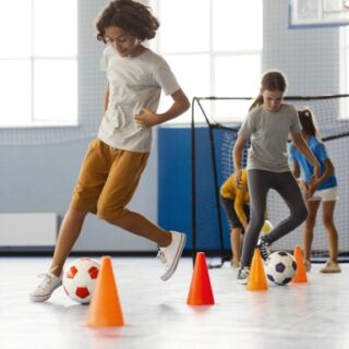 أولاد يتدربون على التحكم بكرة القدم بين قطع مخروطية برتقالية الشكل