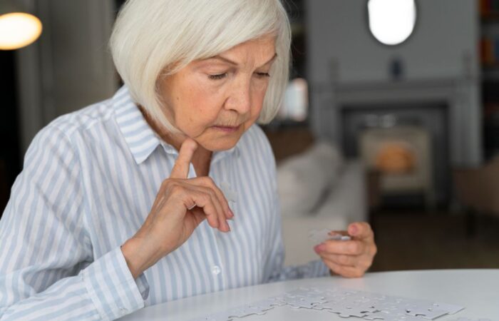 امرأة كبيرة في السن تنظر للعبة البوزل وتضع اصبعا أسفل رأسها