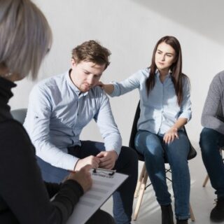 رجل يجلس حزينا ضمن مجموعة من البالغين وتقوم فتاة بوضع يدها على كتفه