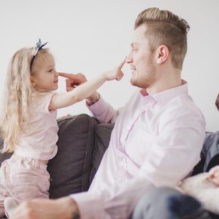 رجل يجلس مع فتاة صغيرة ويضع يده على أنفها وهي تضع يدها على أنفه وخلف الأب يوجد ولد صغير ينظر لهما