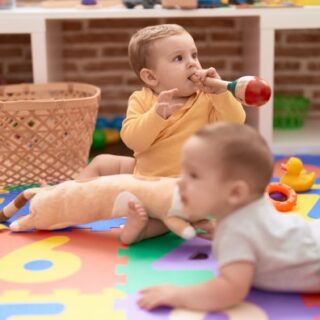 طفل رضيع يزحف على الأرض بجانبه طفل آخر يلعب بالألعاب