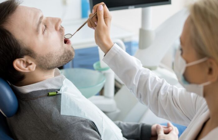 طبيبة أسنان تقوم بفحص أسنان رجل بالغ باستخدام المرآة العاكسة