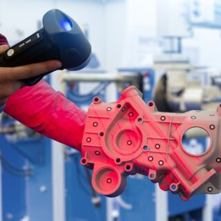 مهندس يمسك جهاز مسح ضوئي ويقوم بتصوير قطعة ميكانيكية حمراء اللون