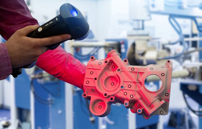 مهندس يمسك جهاز مسح ضوئي ويقوم بتصوير قطعة ميكانيكية حمراء اللون