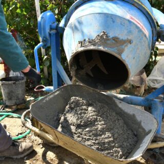 عامل يقوم بتفريغ طين رمادي اللون من قطعة اسطوانية زرقاء داخل عربة نقل يدوية