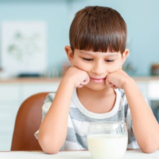 طفل يجلس على طاولة الطعام وأمامه كأس من الحليب