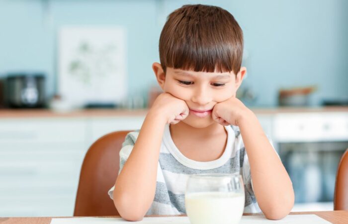 طفل يجلس على طاولة الطعام وأمامه كأس من الحليب