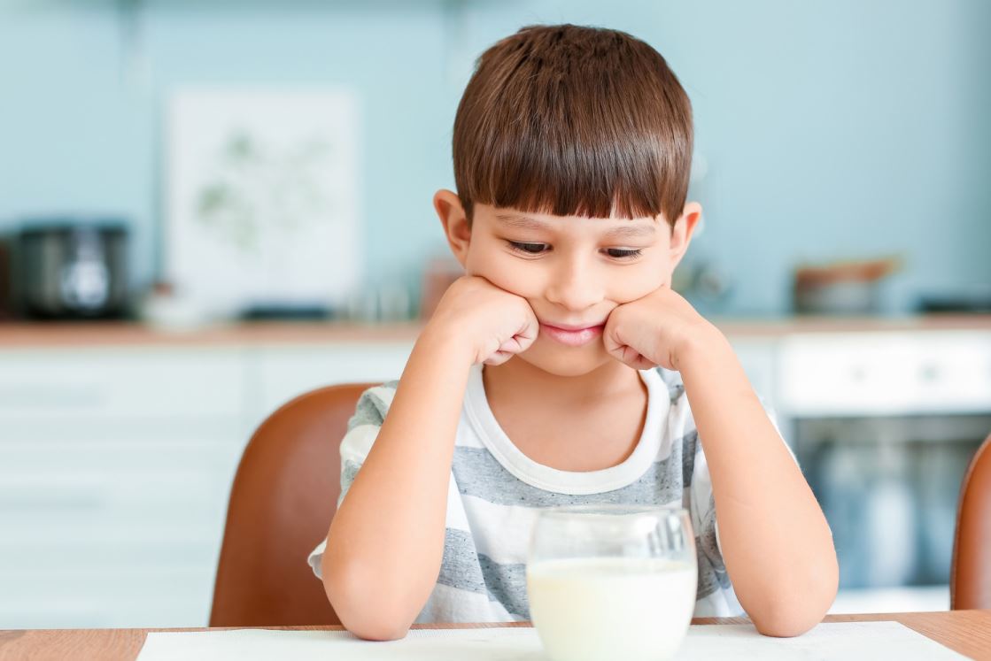 طفل يجلس على طاولة الطعام وأمامه كأس من الحليب
