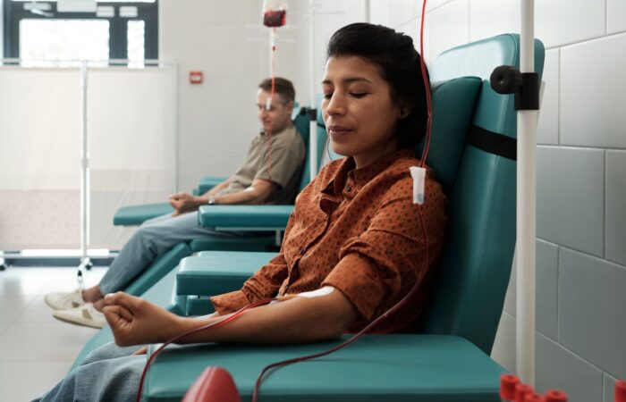 مجموعة من الأشخاص يجلسون على كراسي خضراء ويقومون بالتبرع بالدم في مركز للإسعاف