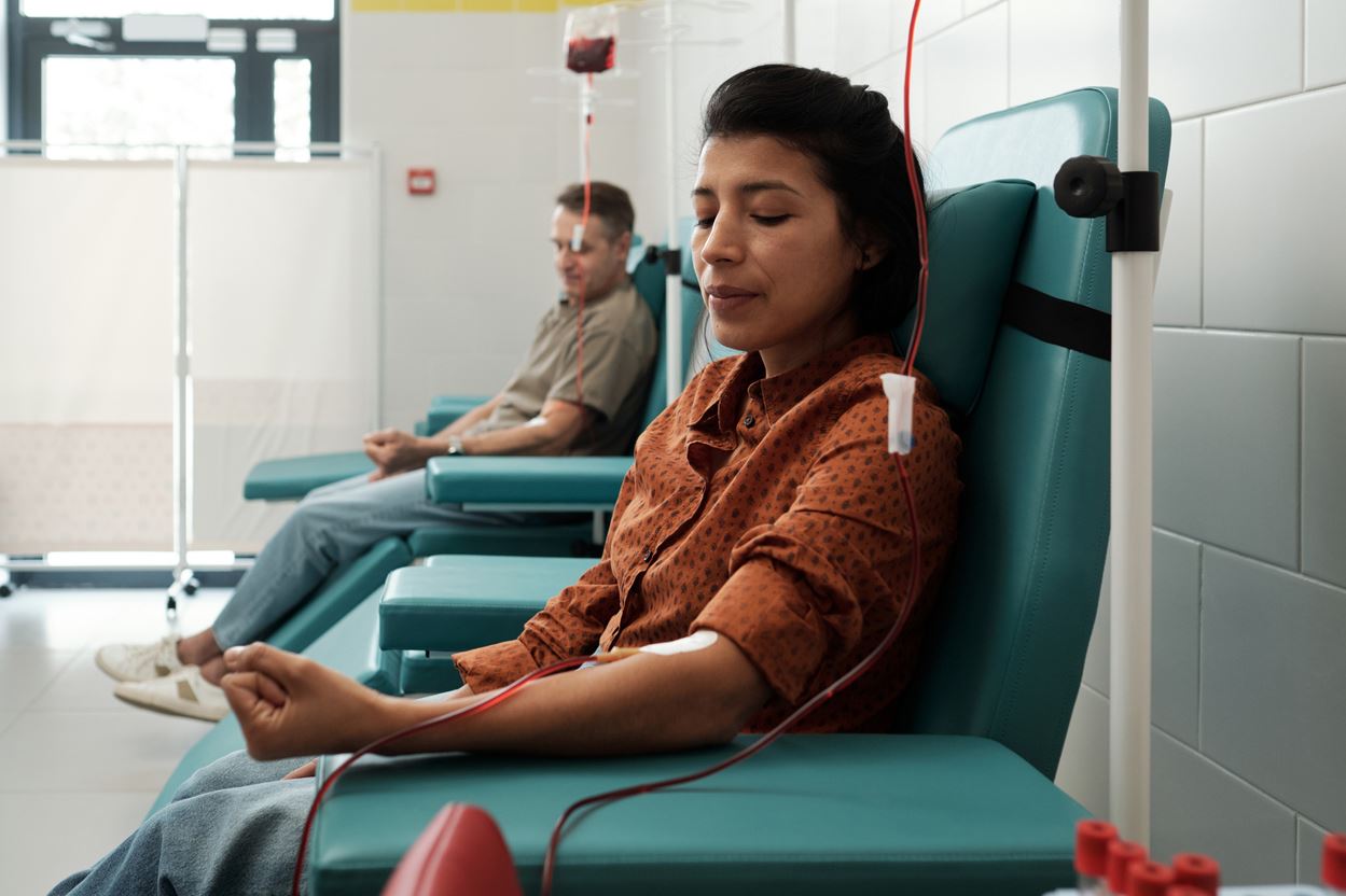 مجموعة من الأشخاص يجلسون على كراسي خضراء ويقومون بالتبرع بالدم في مركز للإسعاف