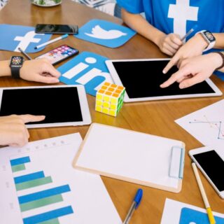 مجموعة من الأشخاص يجلسون حول طاولة بيضاوية الشكل ويوجد عليه جهازين تاب ومجموعة من الأقلام والأوراق