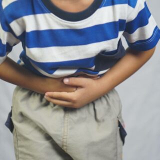 ولد صغير يرتدي كنزة مخططة بالأبيض والأزرق ينحني للأمام ويضع يديه على بطنه