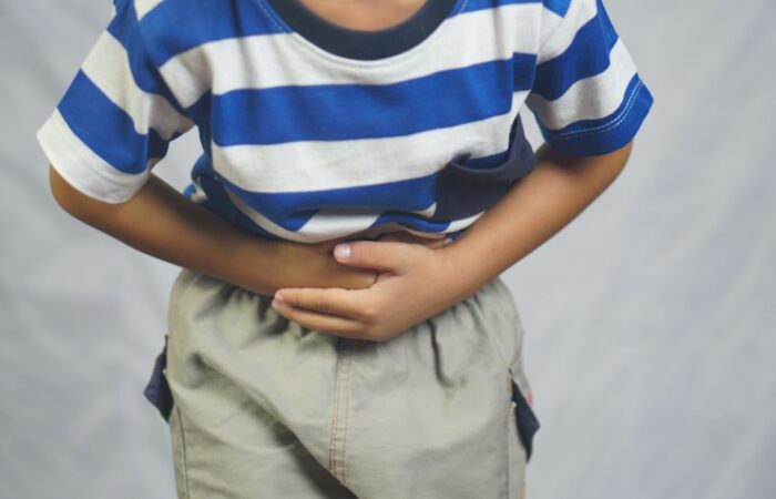 ولد صغير يرتدي كنزة مخططة بالأبيض والأزرق ينحني للأمام ويضع يديه على بطنه