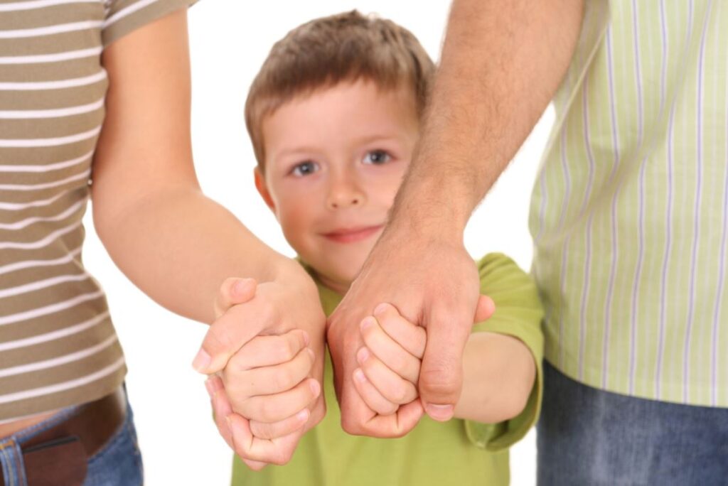 صبي صغير يرتدي كنزة خضراء ويمسك بيدي أبويه