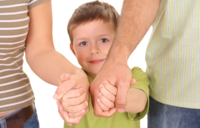 صبي صغير يرتدي كنزة خضراء ويمسك بيدي أبويه