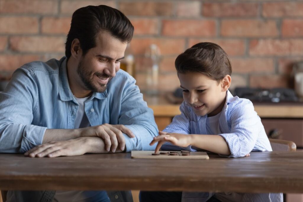 رجل بالغ يجلس بجانب صبي صغير يلعب لعبة موجودة على الطاولة