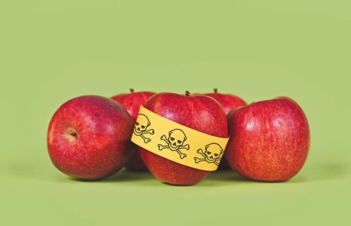 خمس تفاحات حمراء بجانب بعضهم البعض وعلى إحداها يوجد شريط أصفر عليه رسمة لجمجمة ملفوف حولها